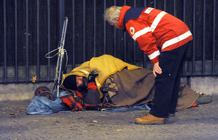 Rot-Kreuz-Mitarbeiter kümmert sich um am Boden liegenden Obdachlosen